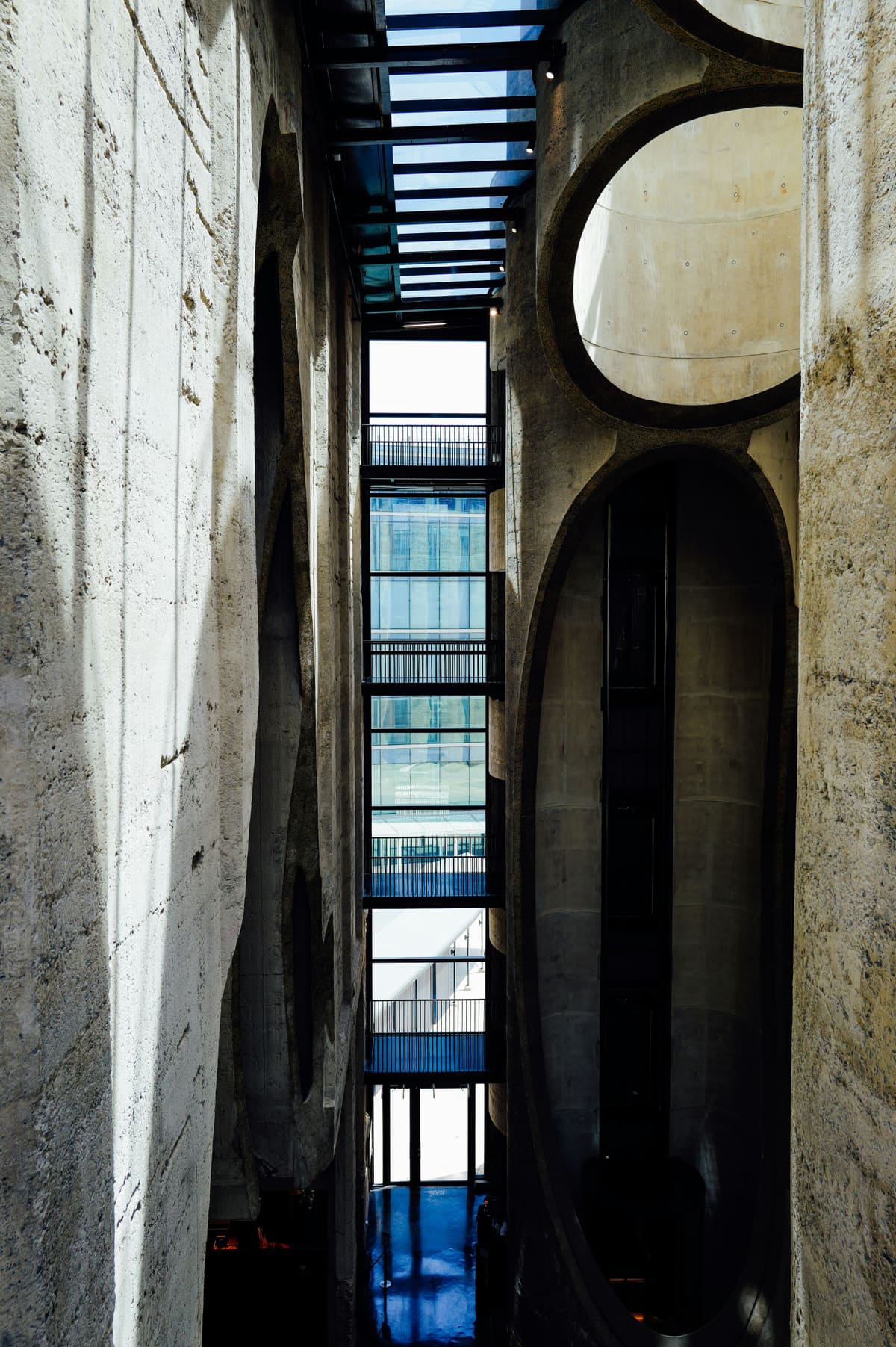 A narrow canyon between raw concrete walls with large oval cut-outs and deep vertical shadow.