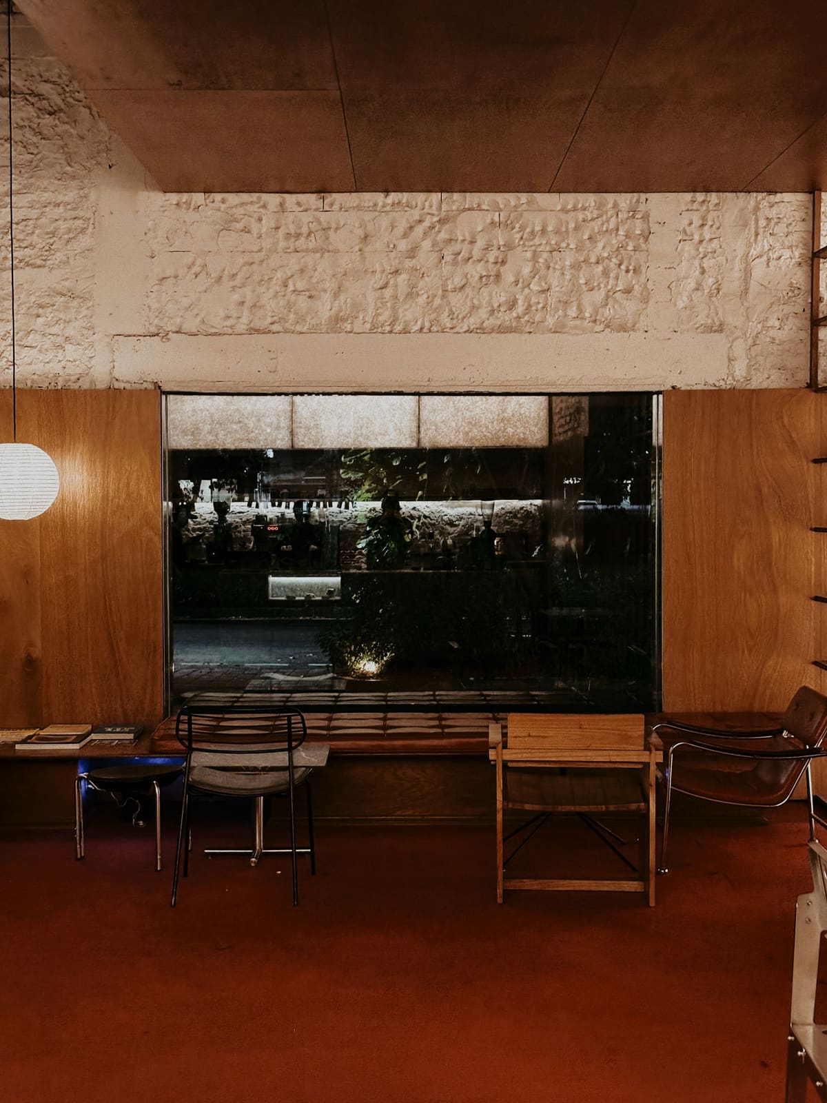 A 1970s material interior: rust floor, timber ceiling, chrome-and-leather chairs, a garden window.