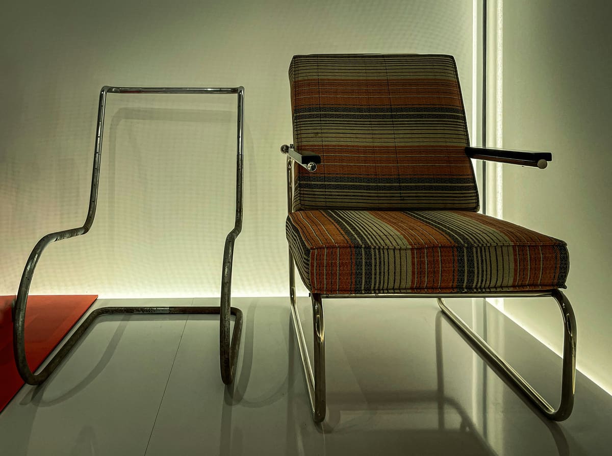 Chrome tubular cantilever chairs, one in plaid upholstery, in warm low light.