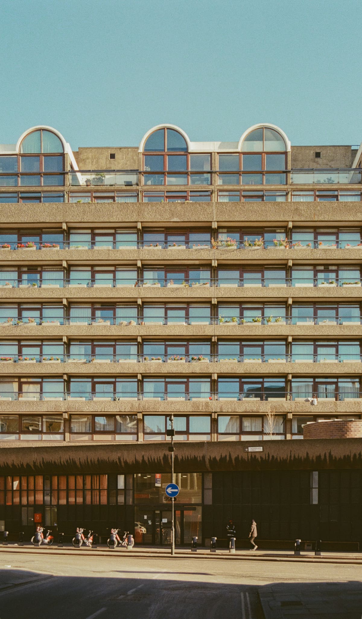 A repeating 1970s modernist concrete facade with arched top-floor windows under a clear blue sky.