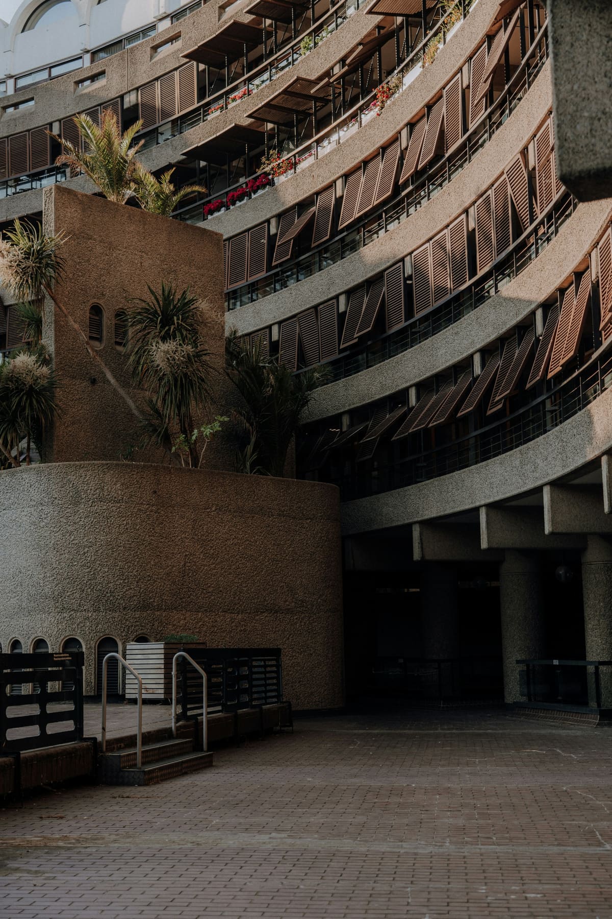 Curving brutalist residential balconies in brown concrete with tropical planting and a dark archway below.