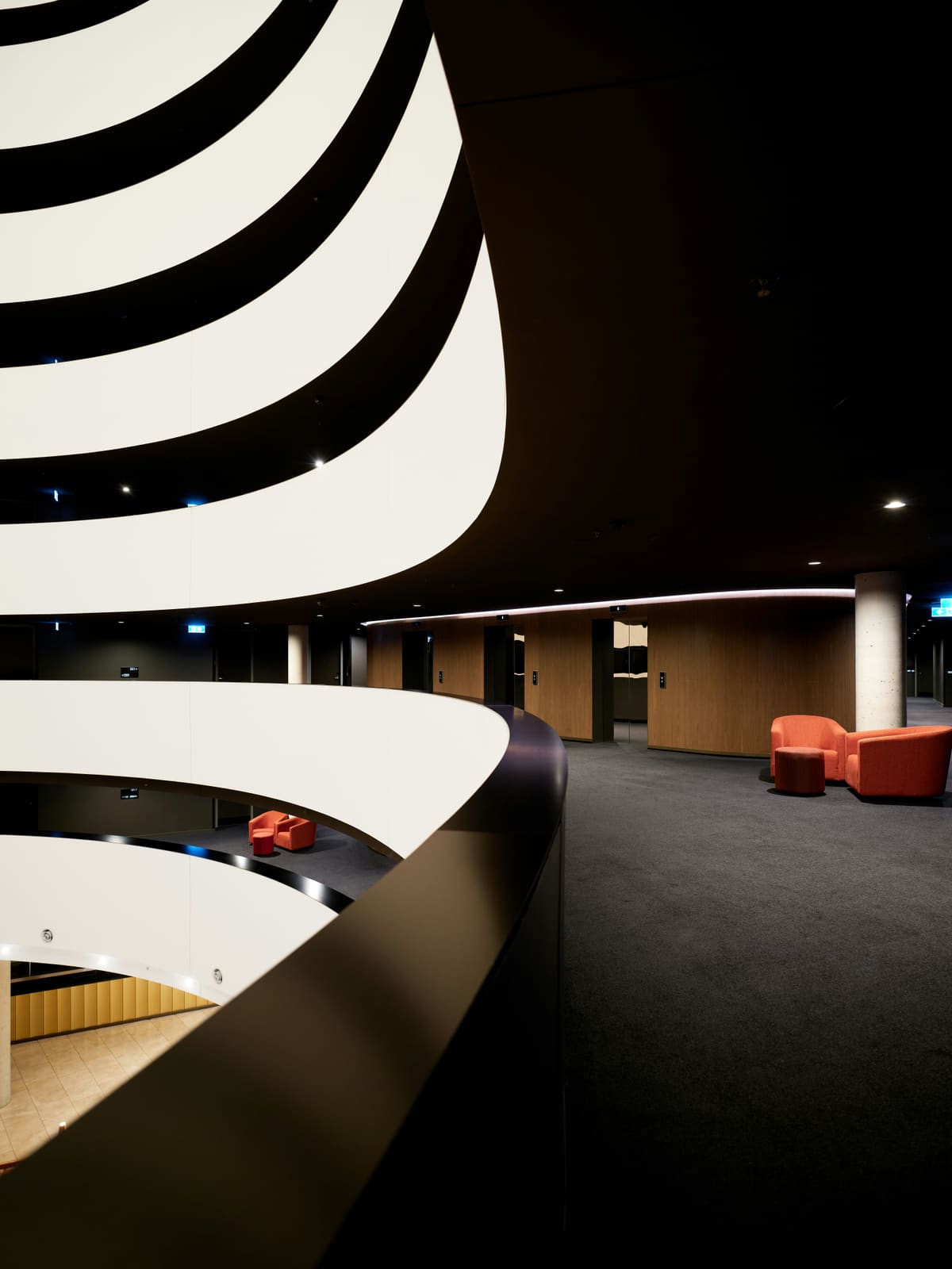 Black-and-white curved ceiling bands over a dark room with a single orange seat.