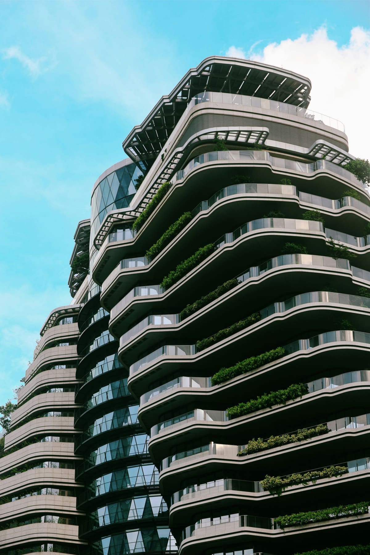 A curved residential tower with plant-filled balconies against a bright blue sky.